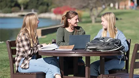 Three female students studying together and laughing at table outside.