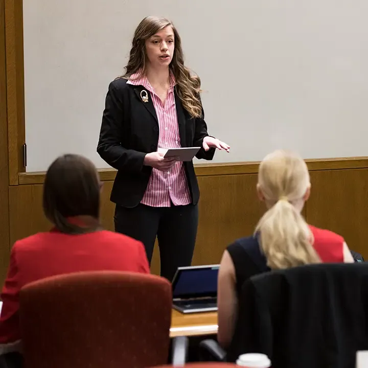 Woman speaking in front of a classroom.